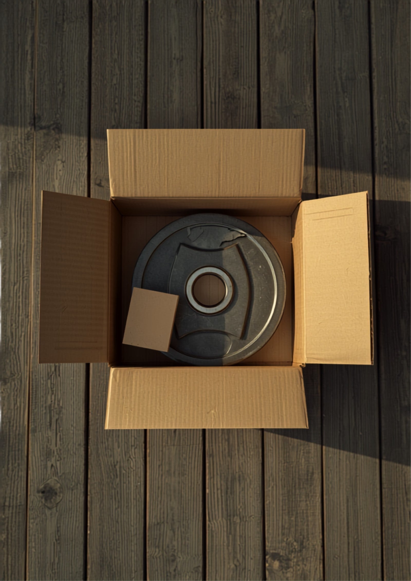Damaged fitness equipment shipping box with a dented metal component next to a sealed supplement subscription box on a front porch.