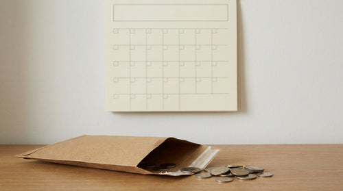 An open return mailer beside a few coins and a blank wall calendar on a desk, representing the cash timeline between refunding a customer and recovering the money.