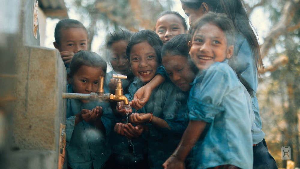 Children gathered around a water faucet in a rural setting
